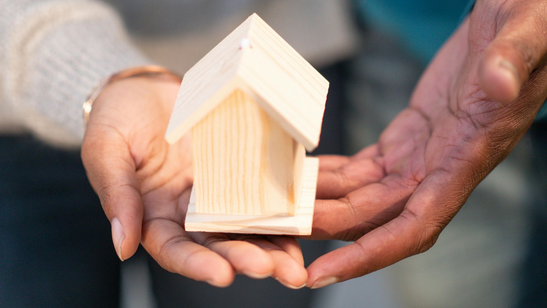 Close-up of hands holding a small wooden house, representing real estate and new home ownership.
