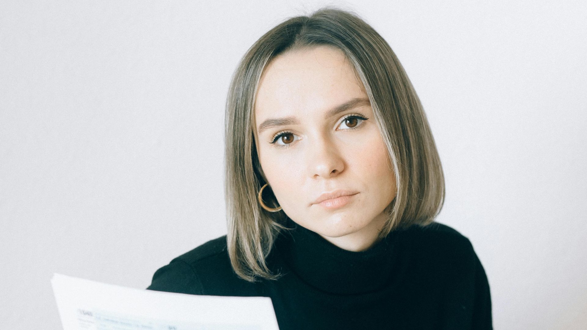 Caucasian woman in black sweater reviewing documents at a desk with paperwork and a laptop.