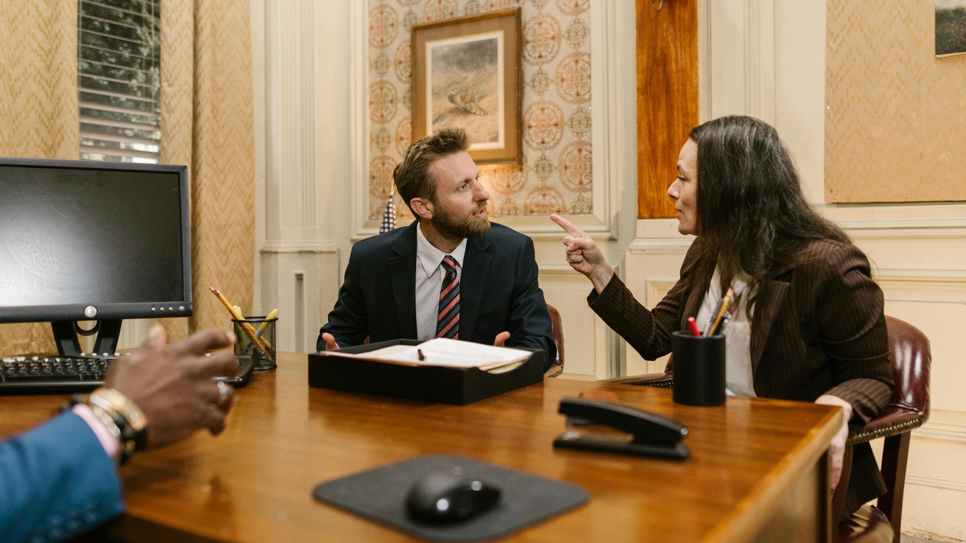 Professionals engaged in a serious discussion inside a law office with a computer on the desk.
