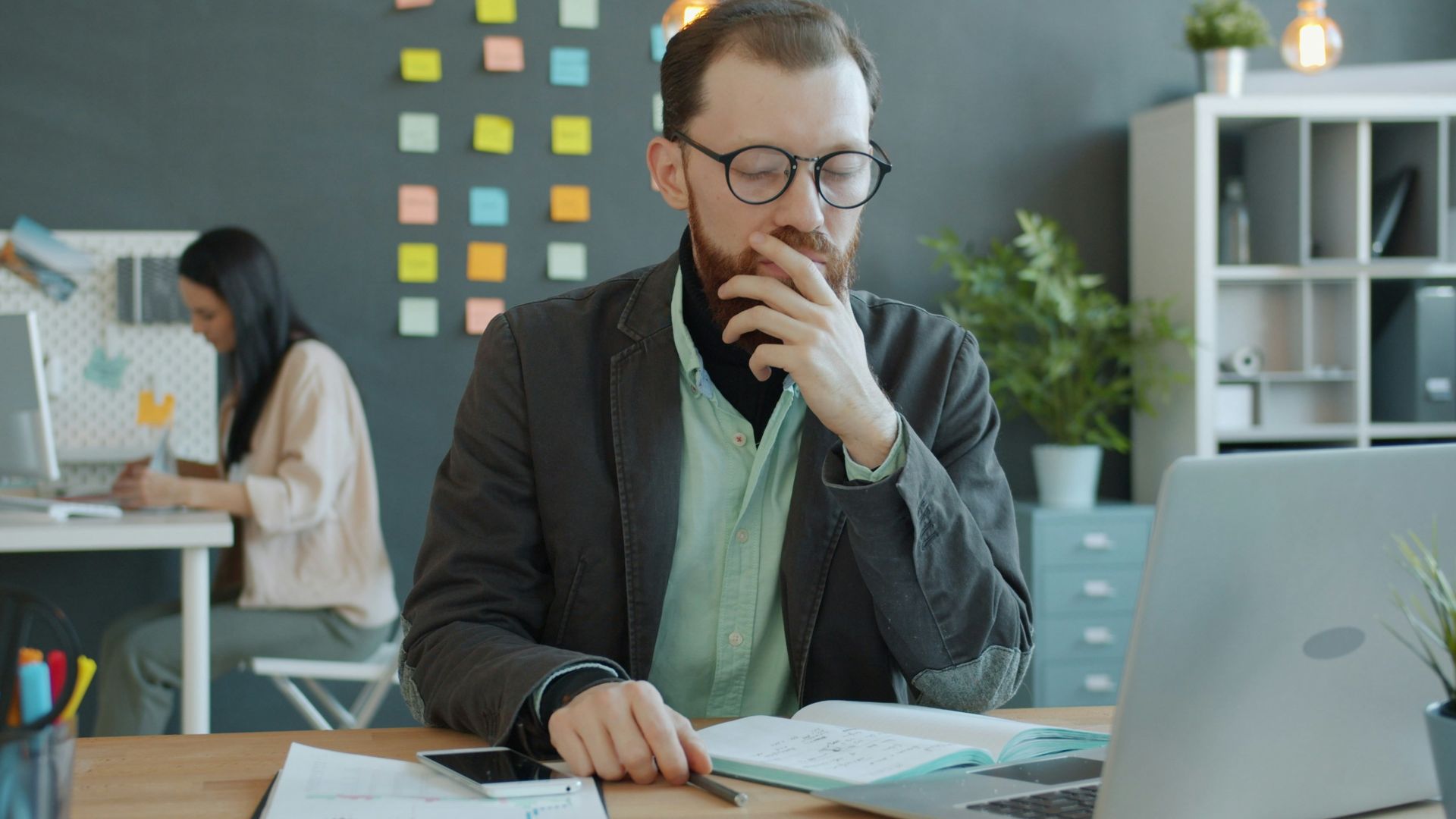 Man thinking at desk with laptop and papers.
