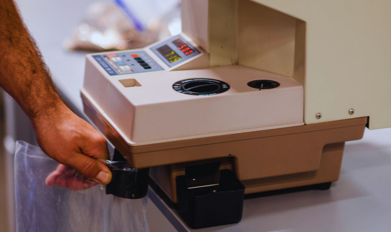 Man filling a plastic bag with metal coins after counting them on a electronic machine that is used for counting and sorting