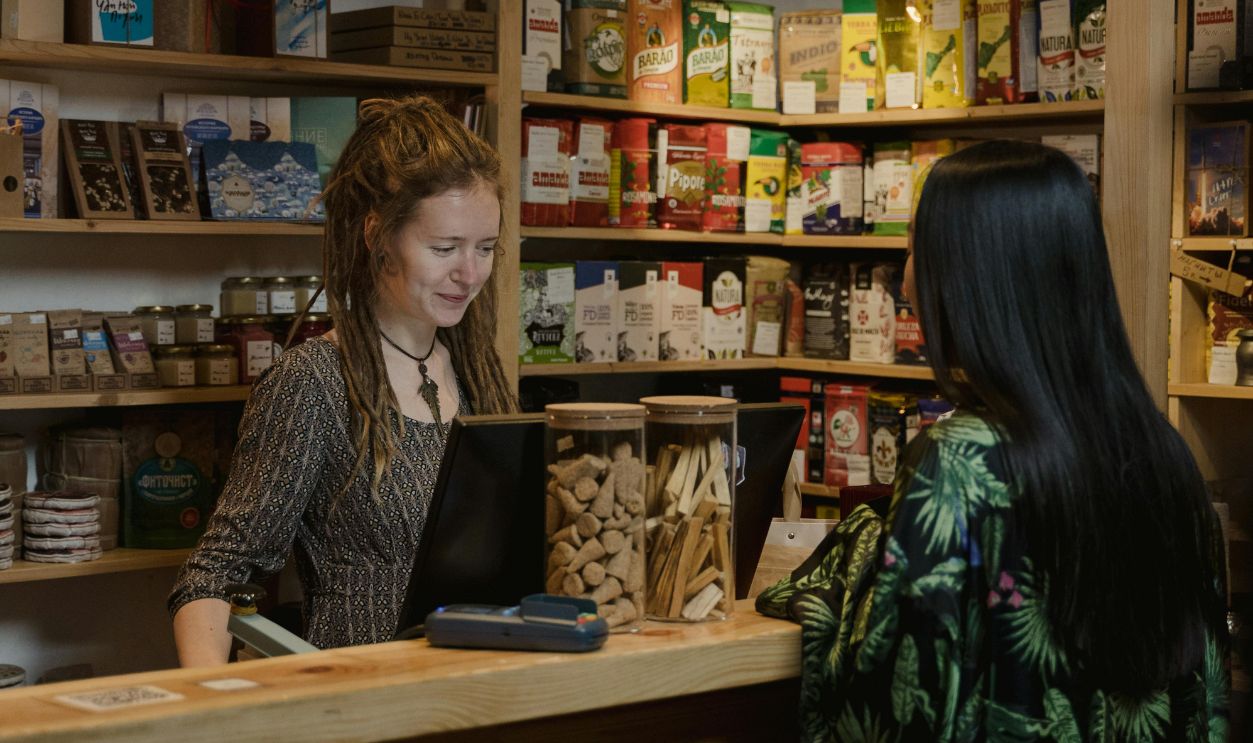 Woman in Tropical Print Dress Ordering in Front of Cashier Behind the Counter