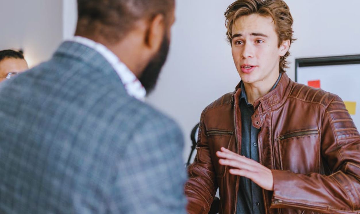 Shallow Focus of a Man Wearing Brown Leather Jacket while Talking to His Colleague