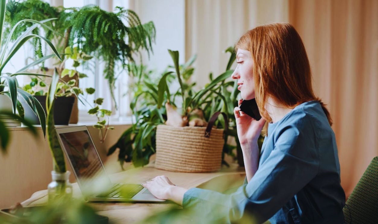 Woman Working on Wooden Table Surrounded with Green Potted Plants
