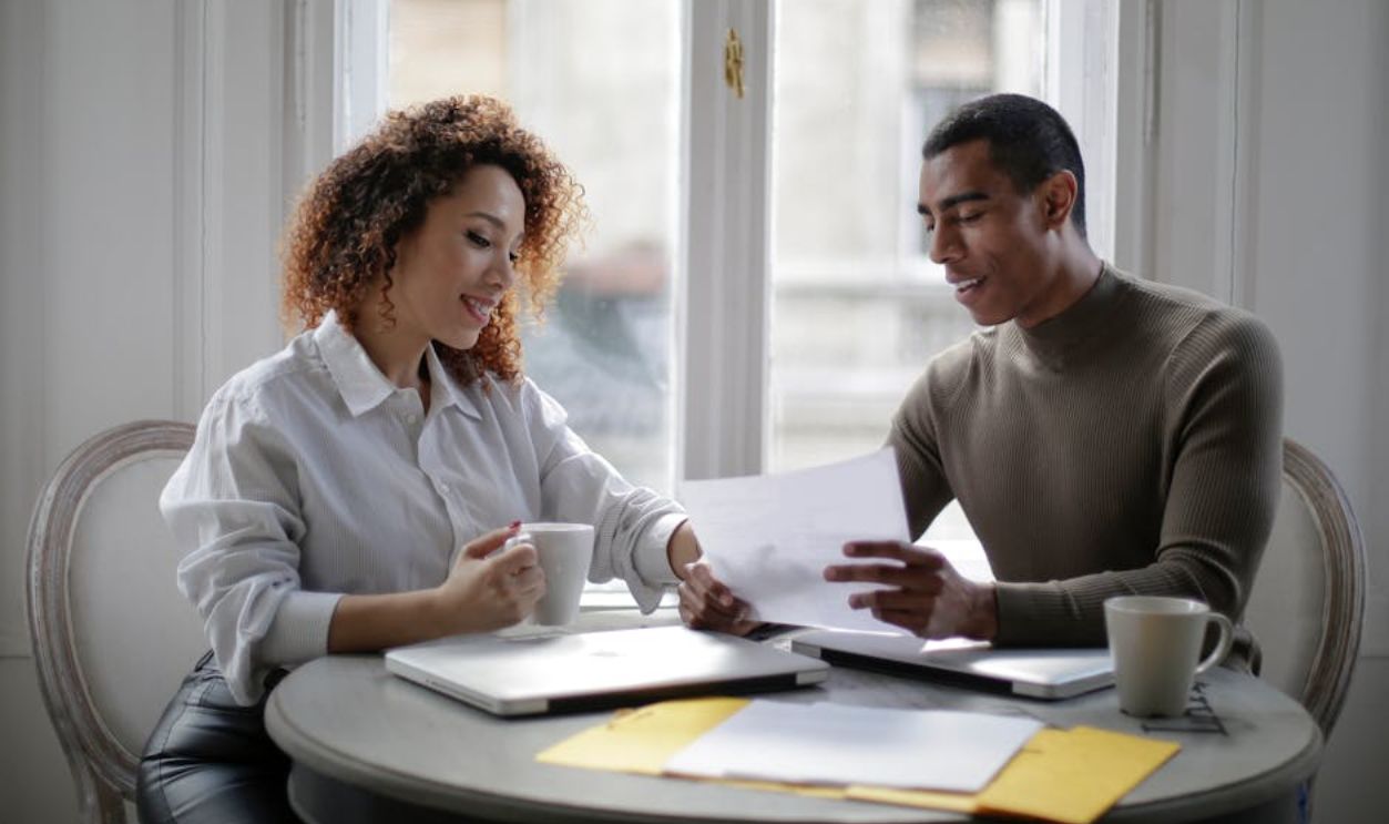 Positive ethnic couple working together with documents while sitting at round table