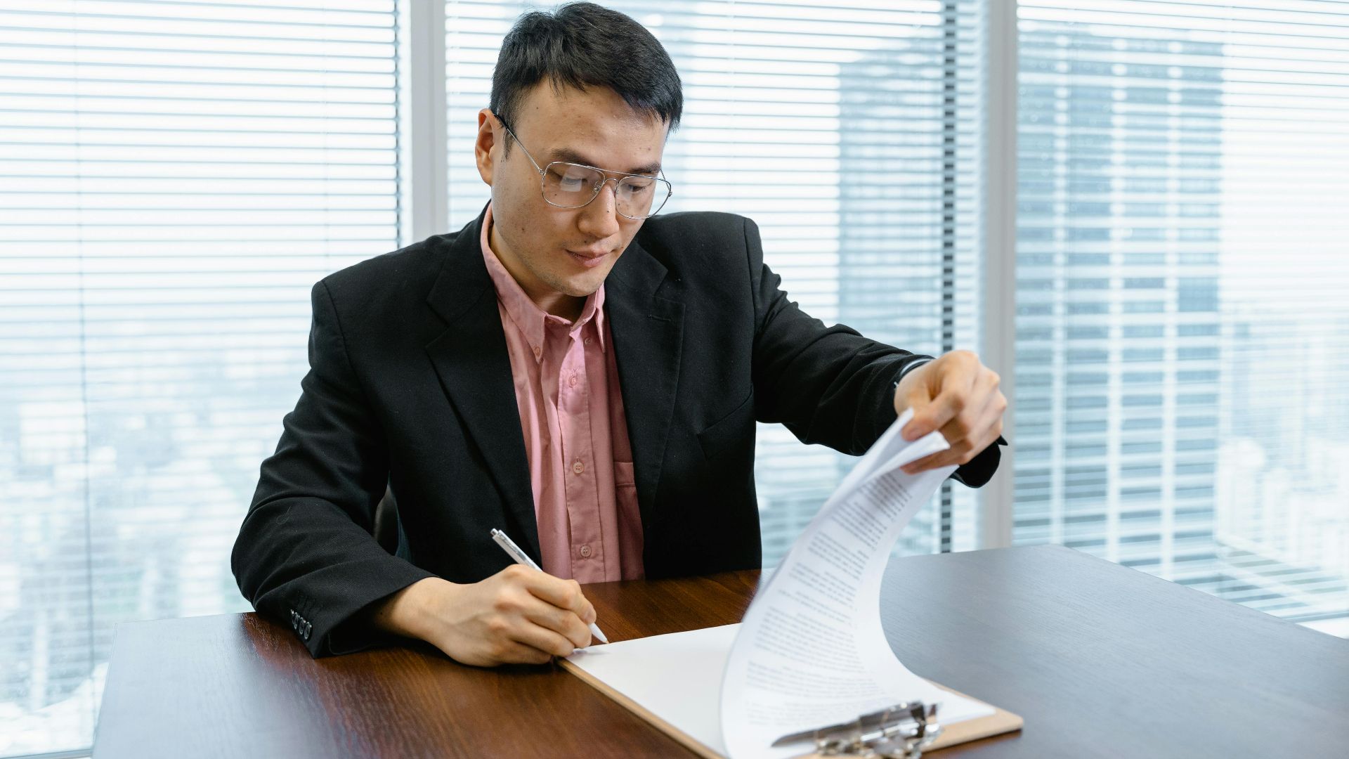 Asian businessman in formal wear signs paperwork at office desk.
