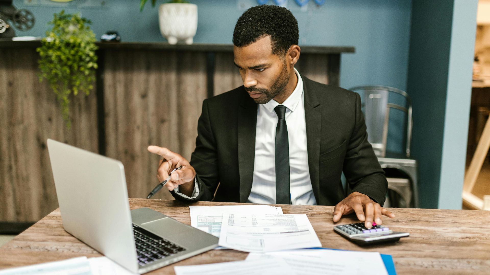 Professional man in a suit using a laptop and calculator in an office setting.