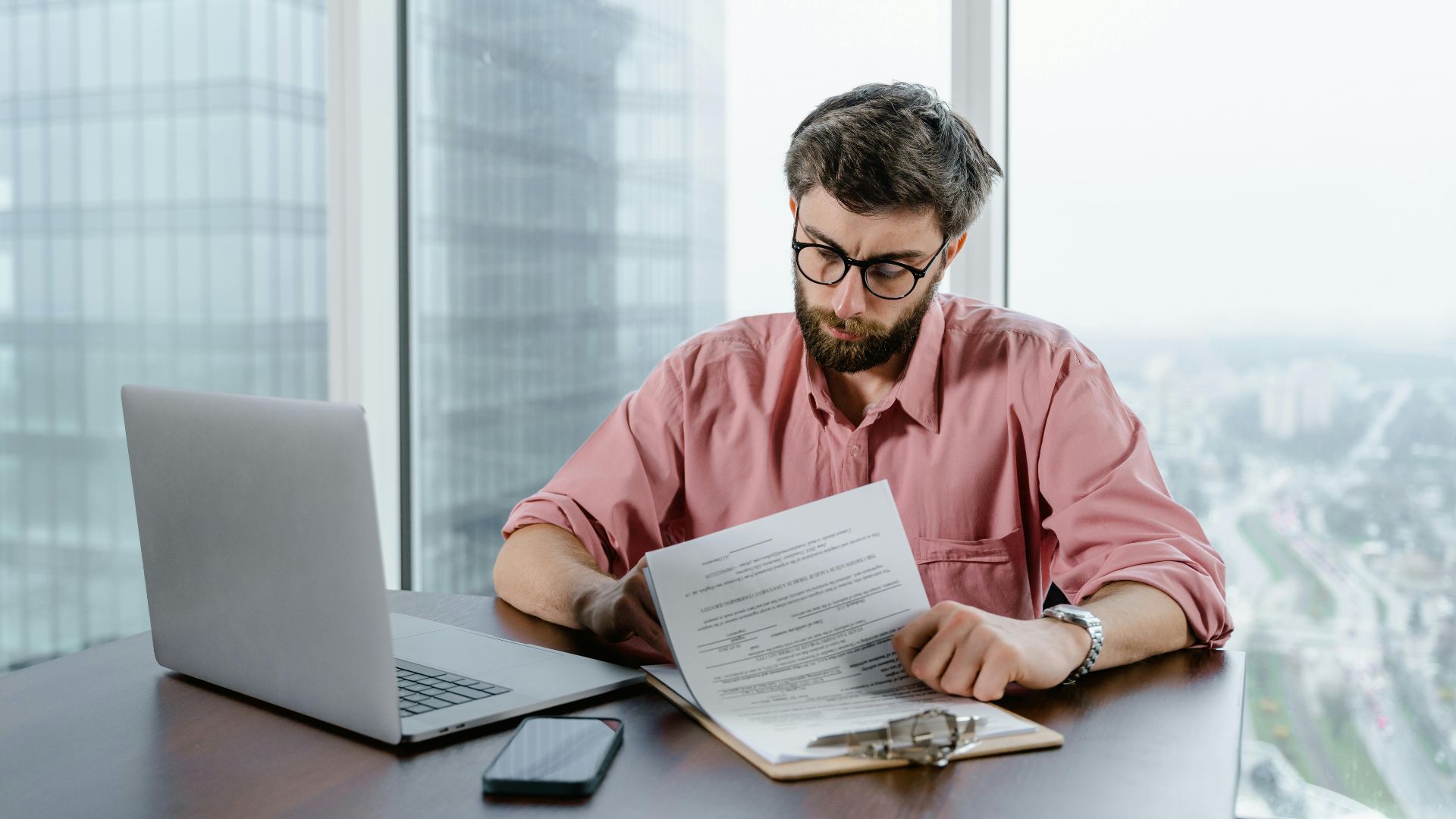 Professional man in pink shirt working with documents at a modern office desk.