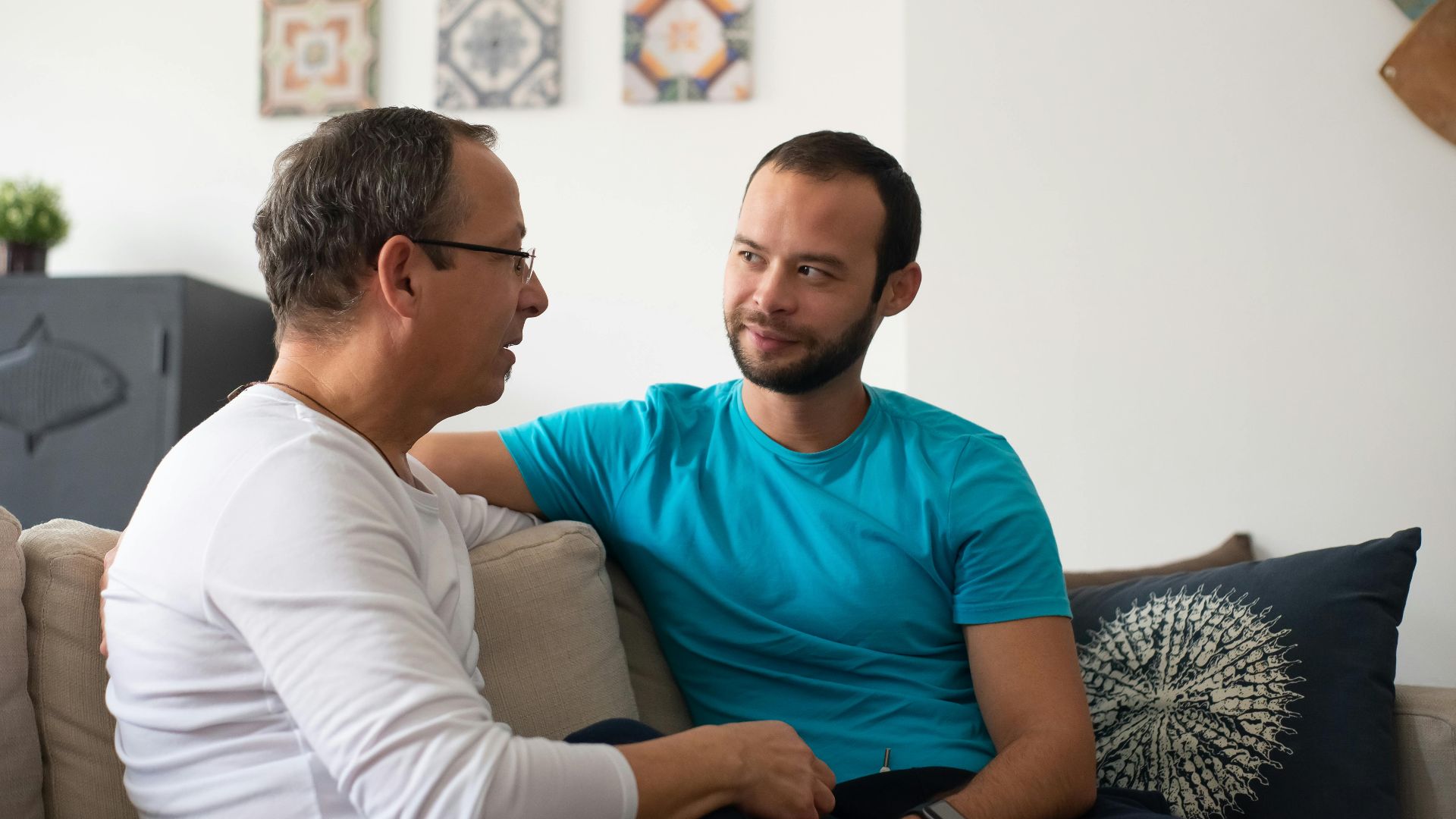 Two men share a heartfelt conversation on a cozy sofa in a modern living room.