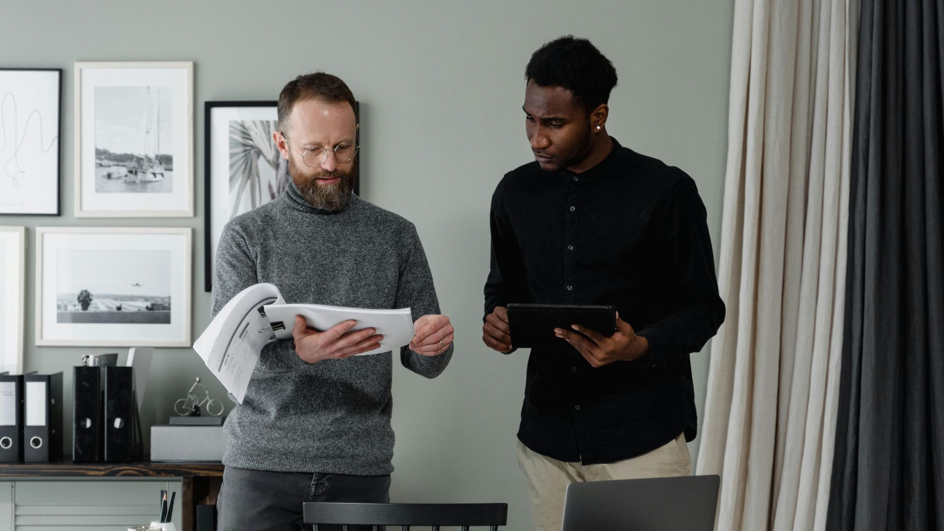 Two professionals reviewing documents and using a tablet in a modern office setting.