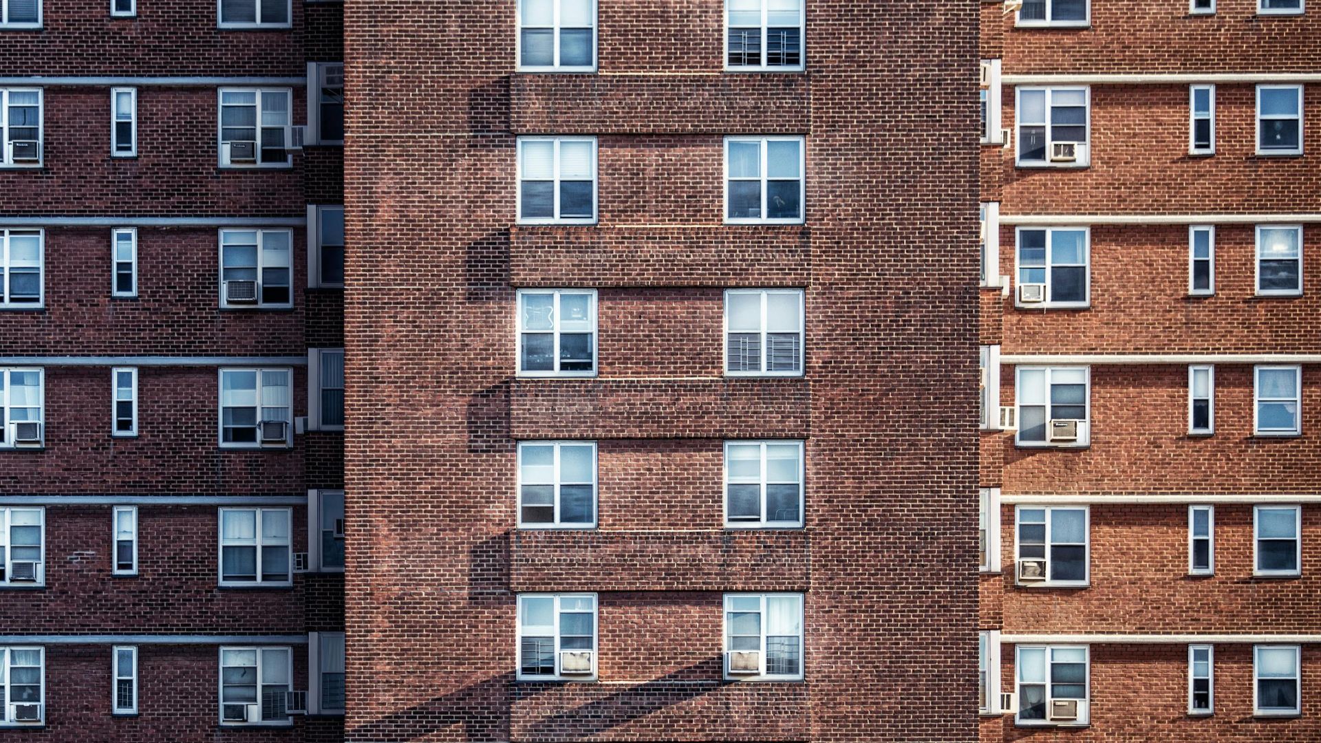 Close-up view of a high-rise brick building facade with multiple windows and air conditioning units.