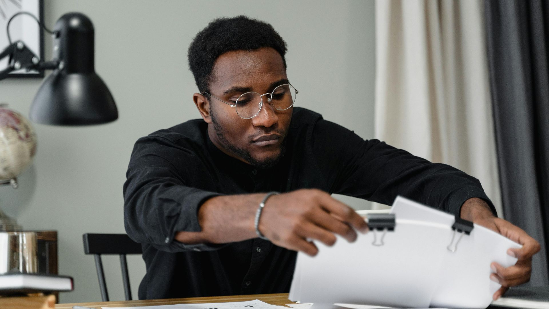 Professional man with glasses reviews documents at a desk in an office setting, emphasizing concentration.