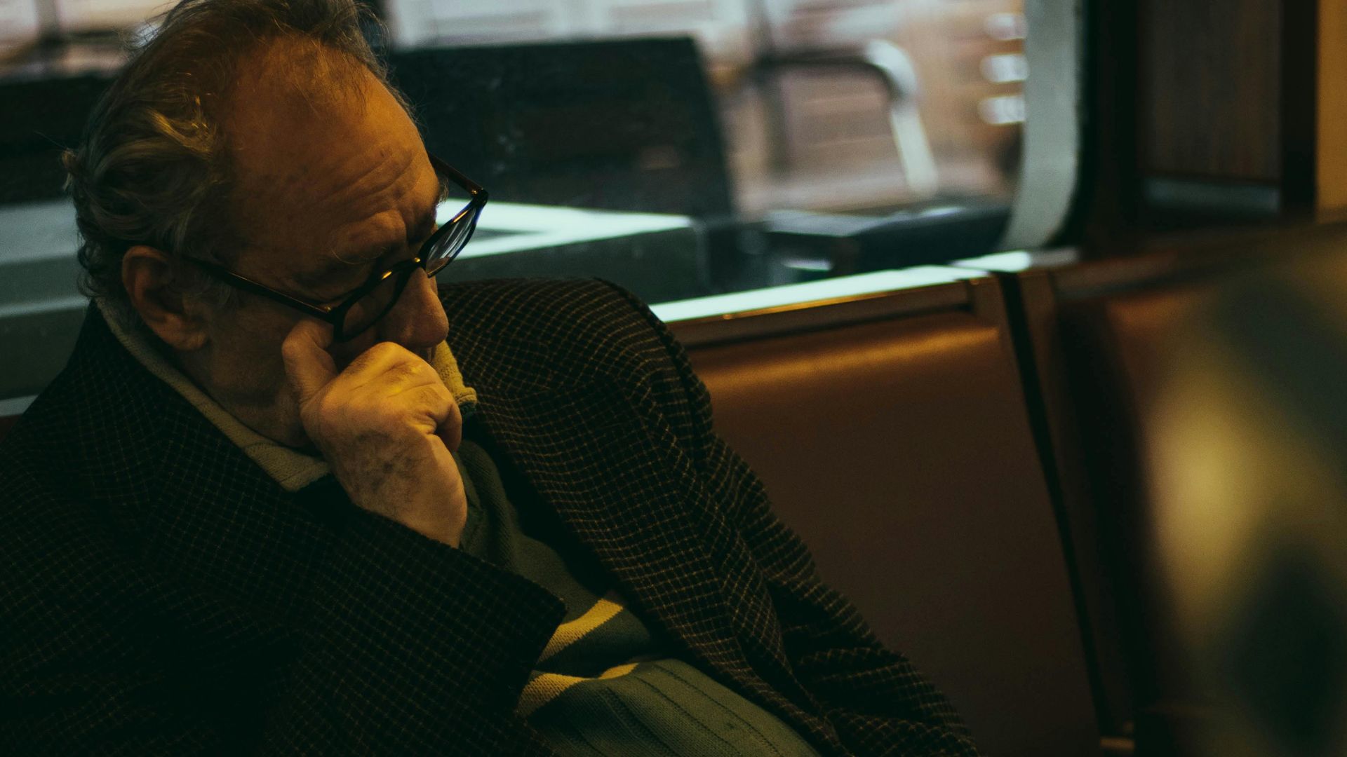 A senior man in glasses resting in a cozy seat on public transport, indoors.