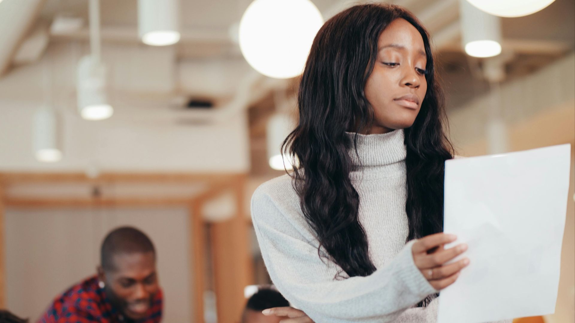 Focused woman examining a paper in a busy office setting.