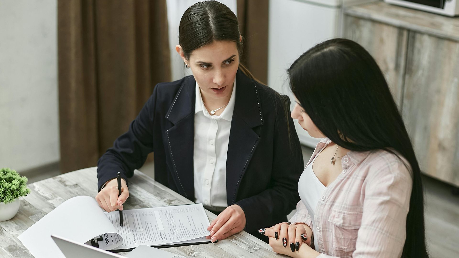 Two businesswomen engaged in a contract discussion at an office table.