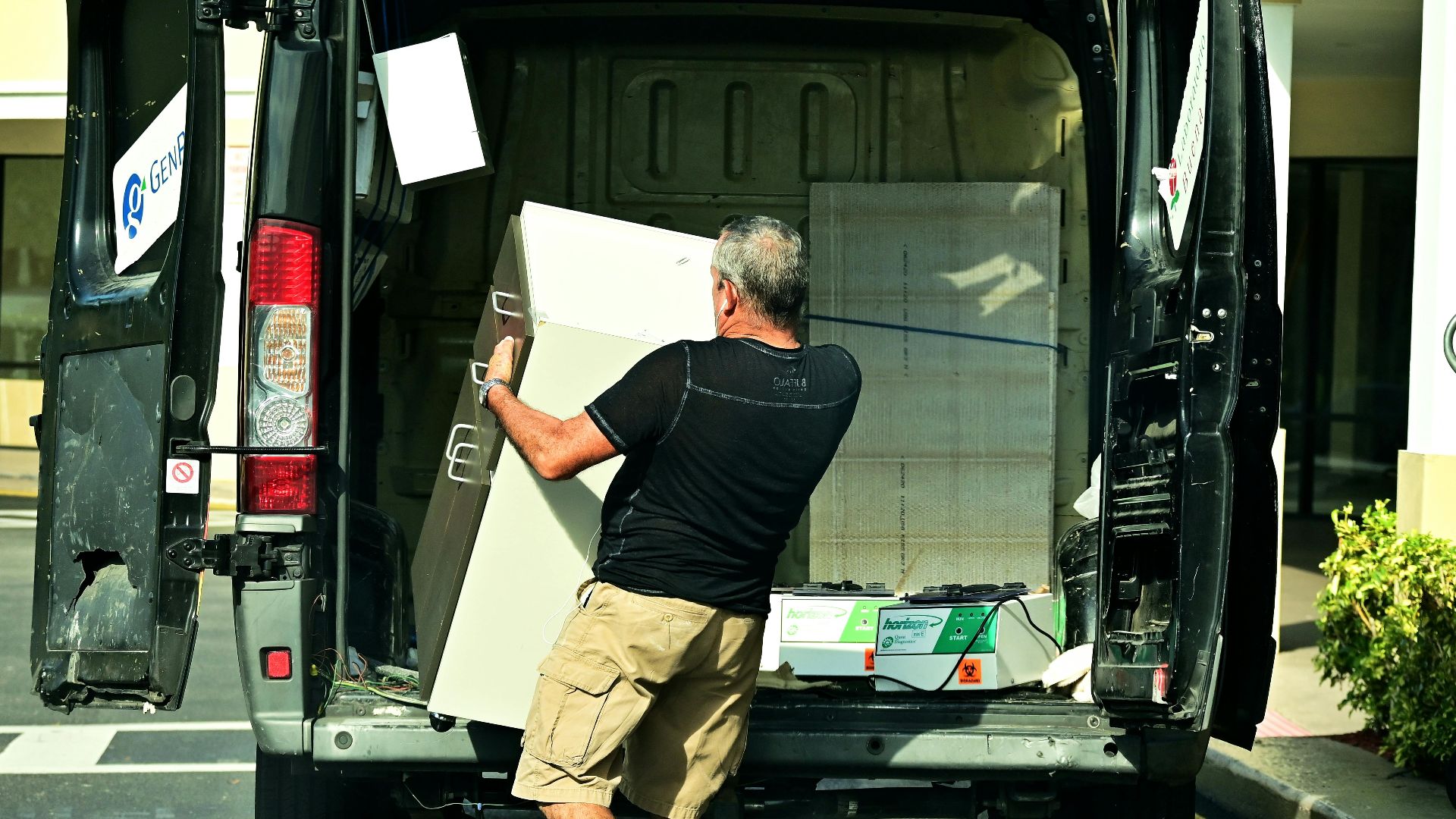 Adult man loading furniture into an open van in a parking lot, daytime setting.