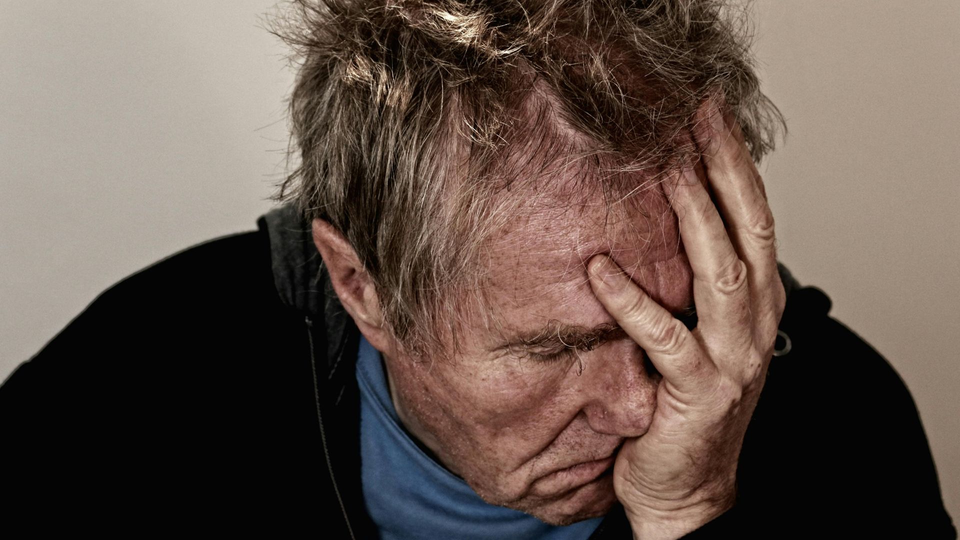 Portrait of an elderly man feeling stress and disappointment, holding his head in his hands.