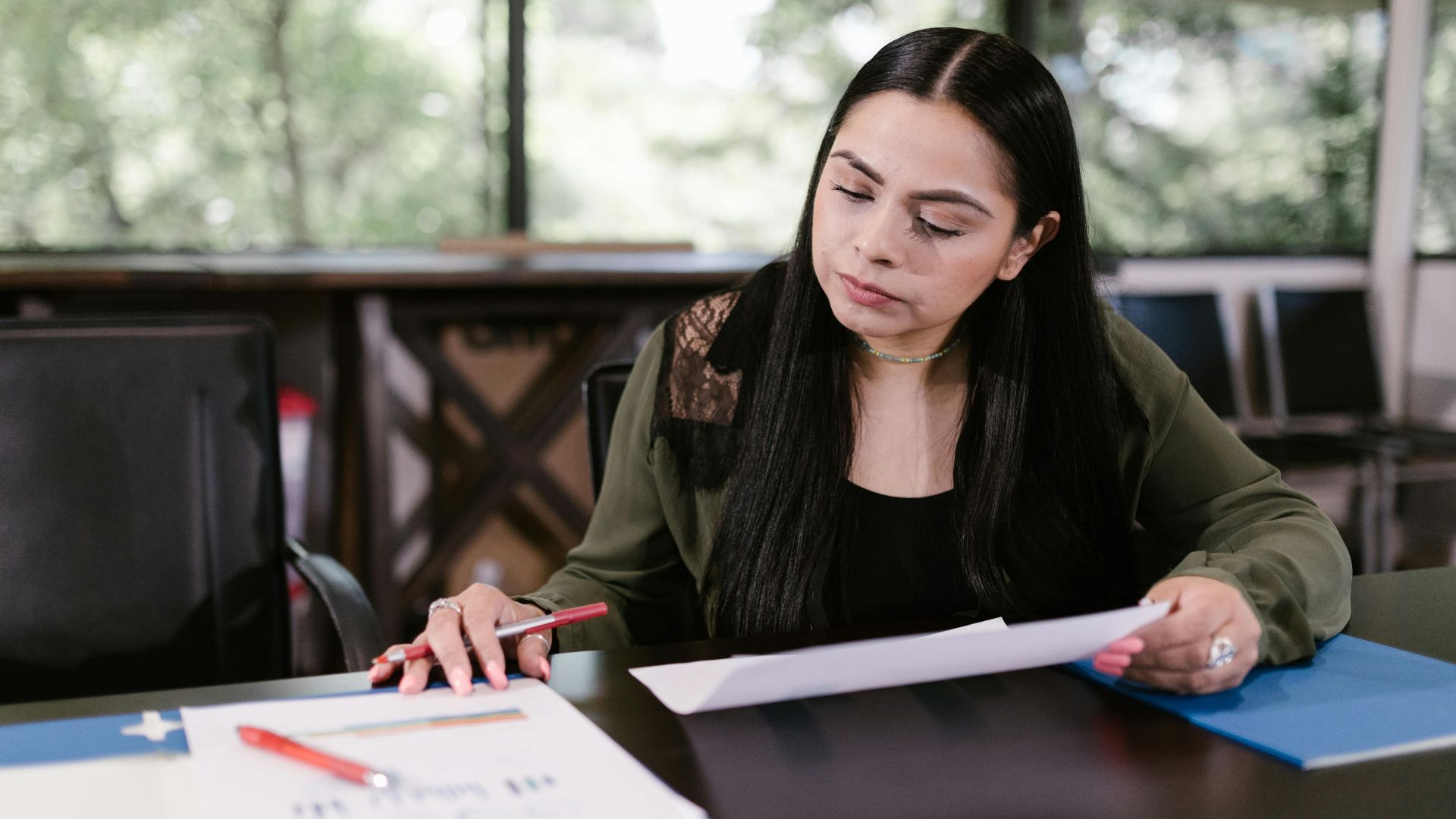 Professional woman in office setting studying documents with concentration.