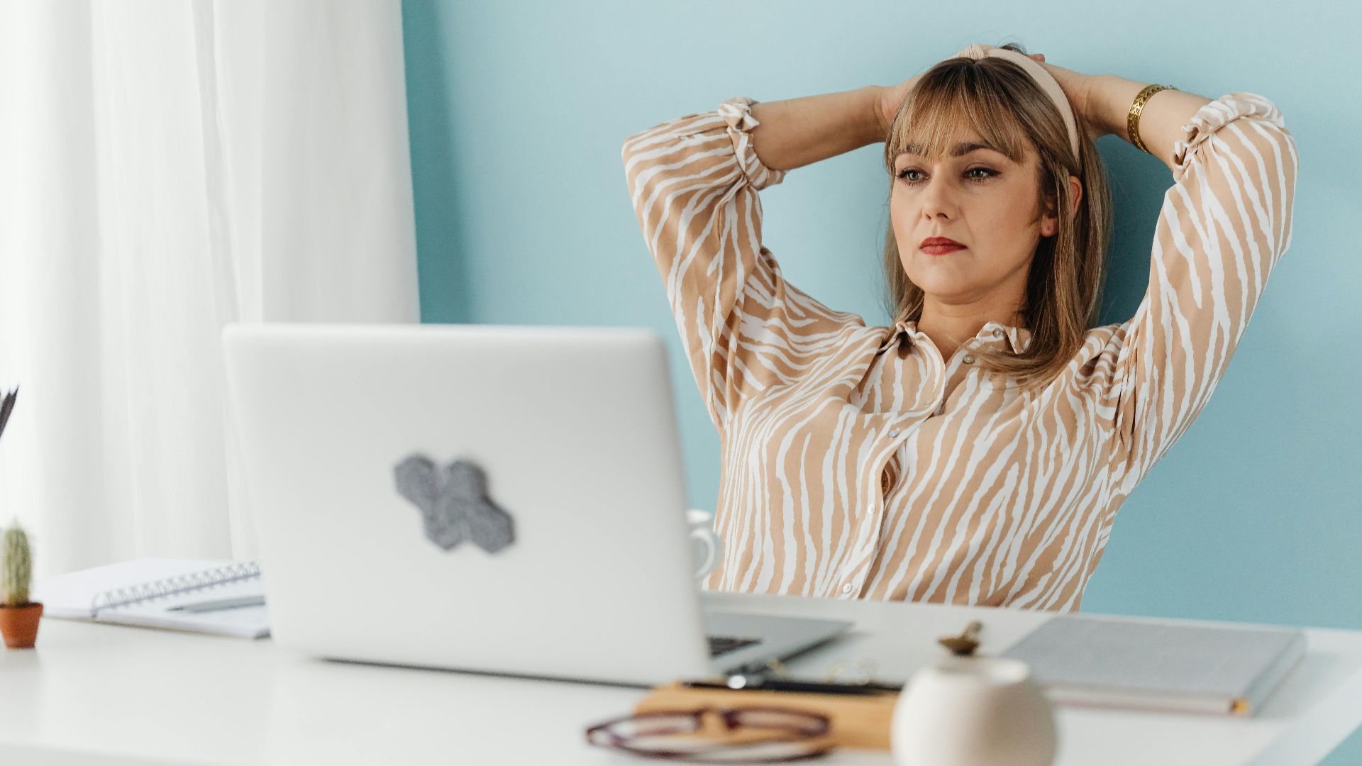 A woman resting at a desk, leaning back with hands behind head, in a home office setting.