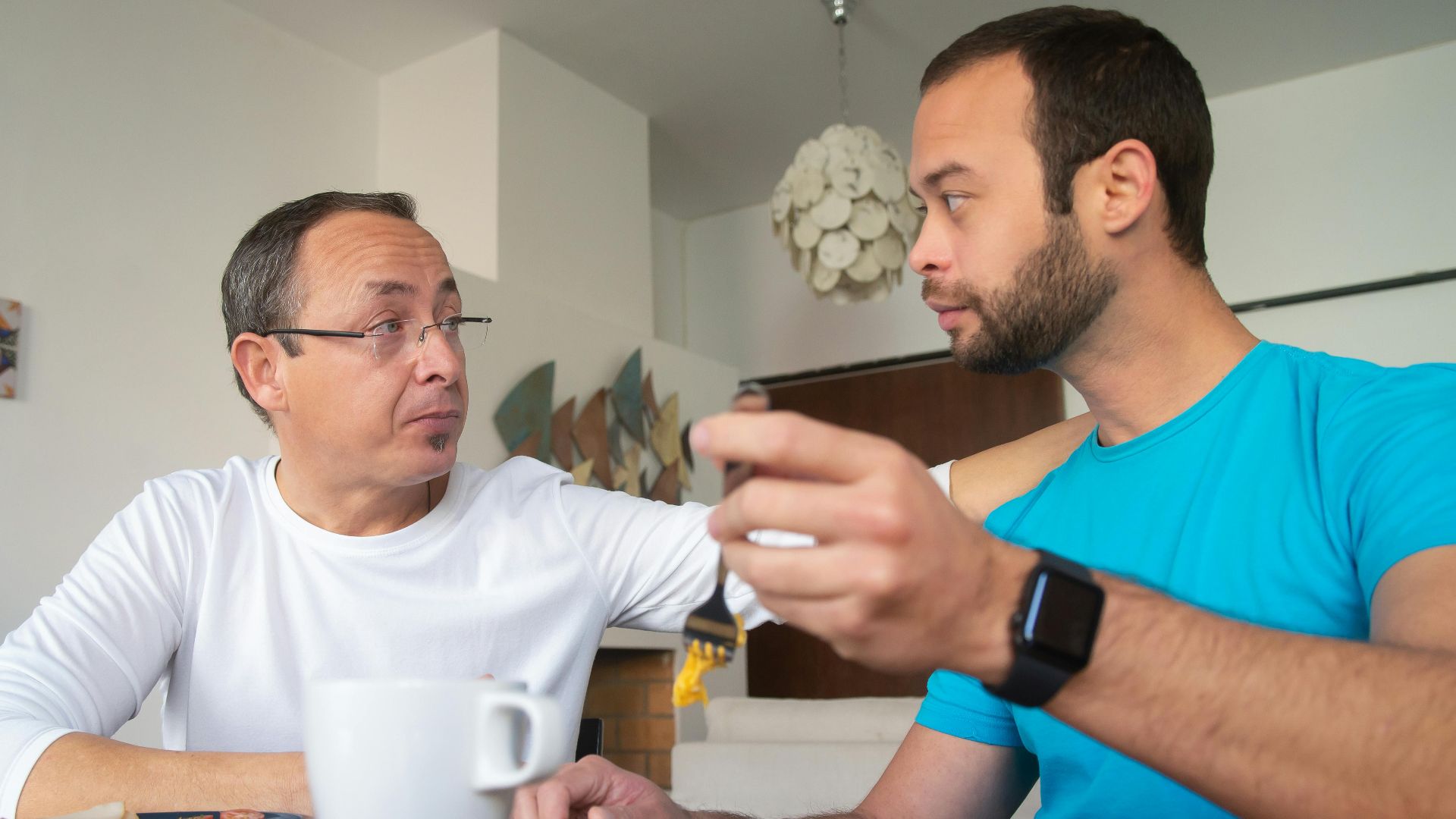 Two men enjoying breakfast together indoors, engaged in a warm conversation.