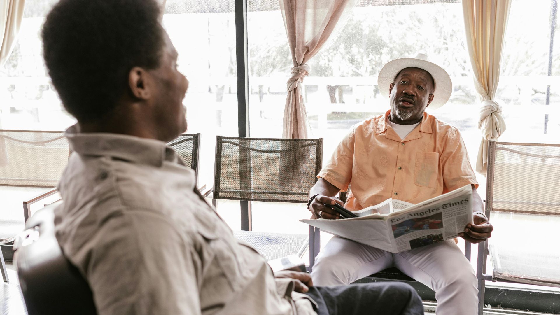 An elderly man and a younger man converse in a modern, well-lit lounge area, enhancing themes of community and relaxation.