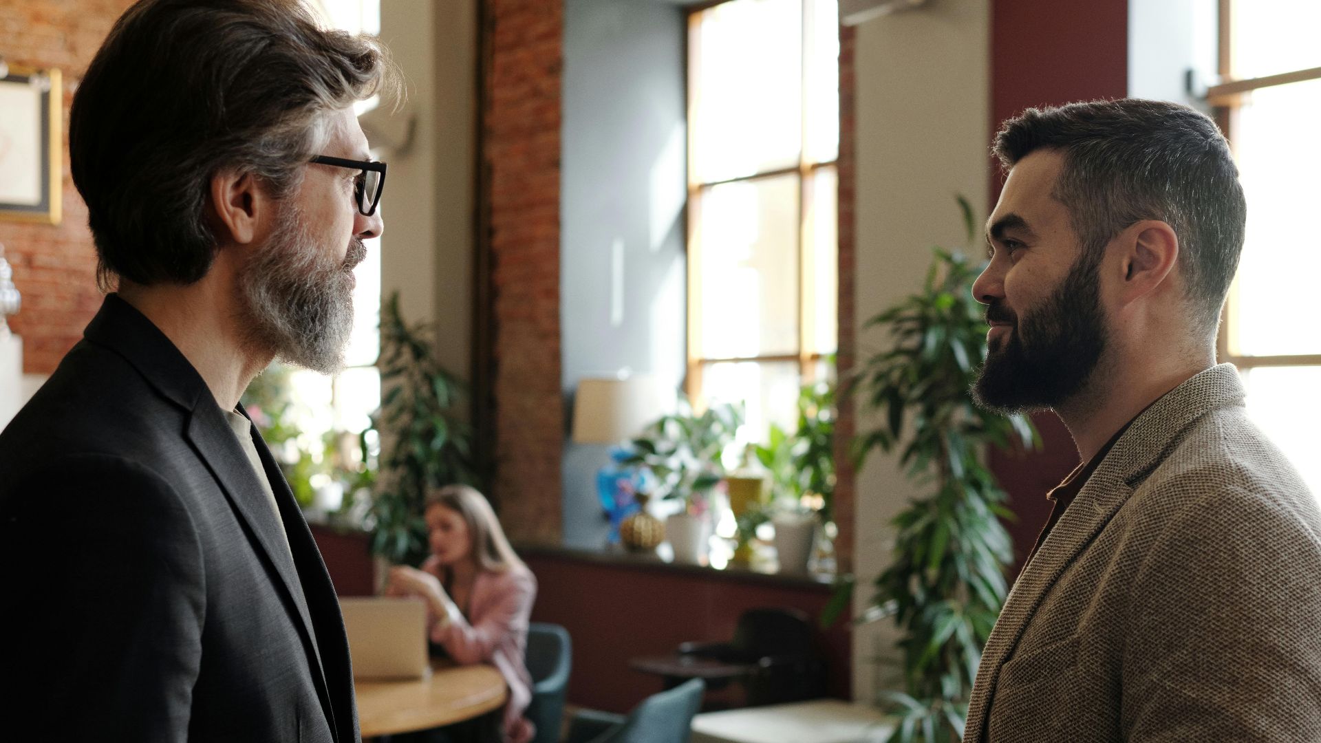 Two bearded men engage in a professional conversation in a stylish cafe interior.