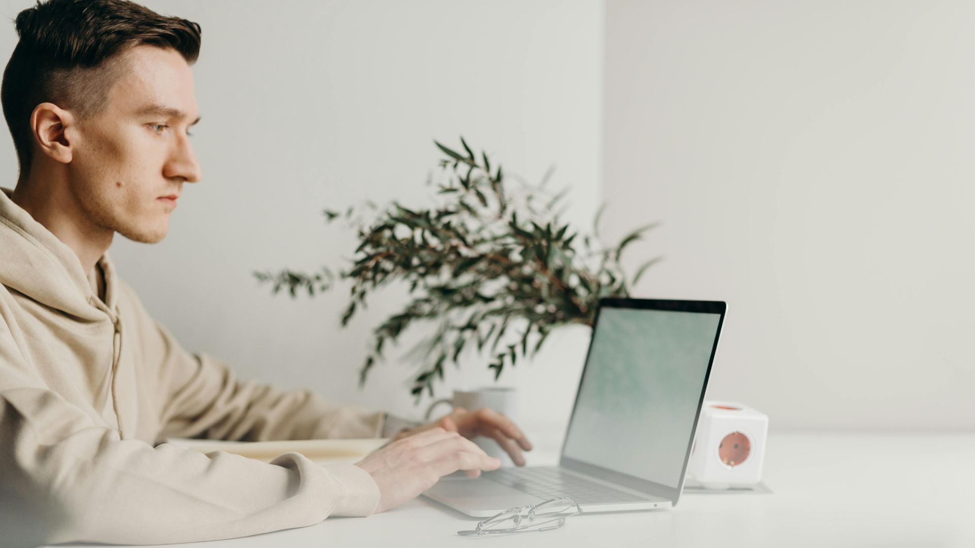 A young man focuses intently on his laptop in a minimalist home office setting.