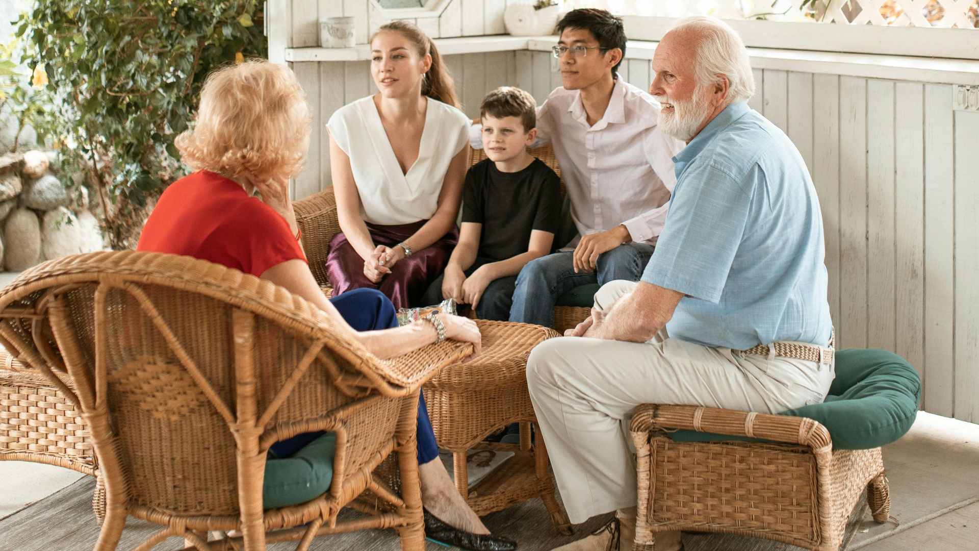 Family enjoys quality time together on cozy outdoor porch with wicker chairs.