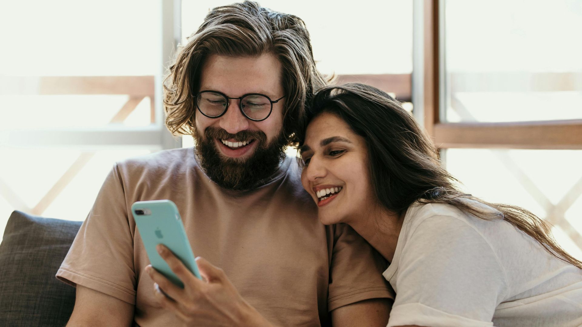 A joyful couple laughing and looking at a phone together in bed, enjoying their morning.