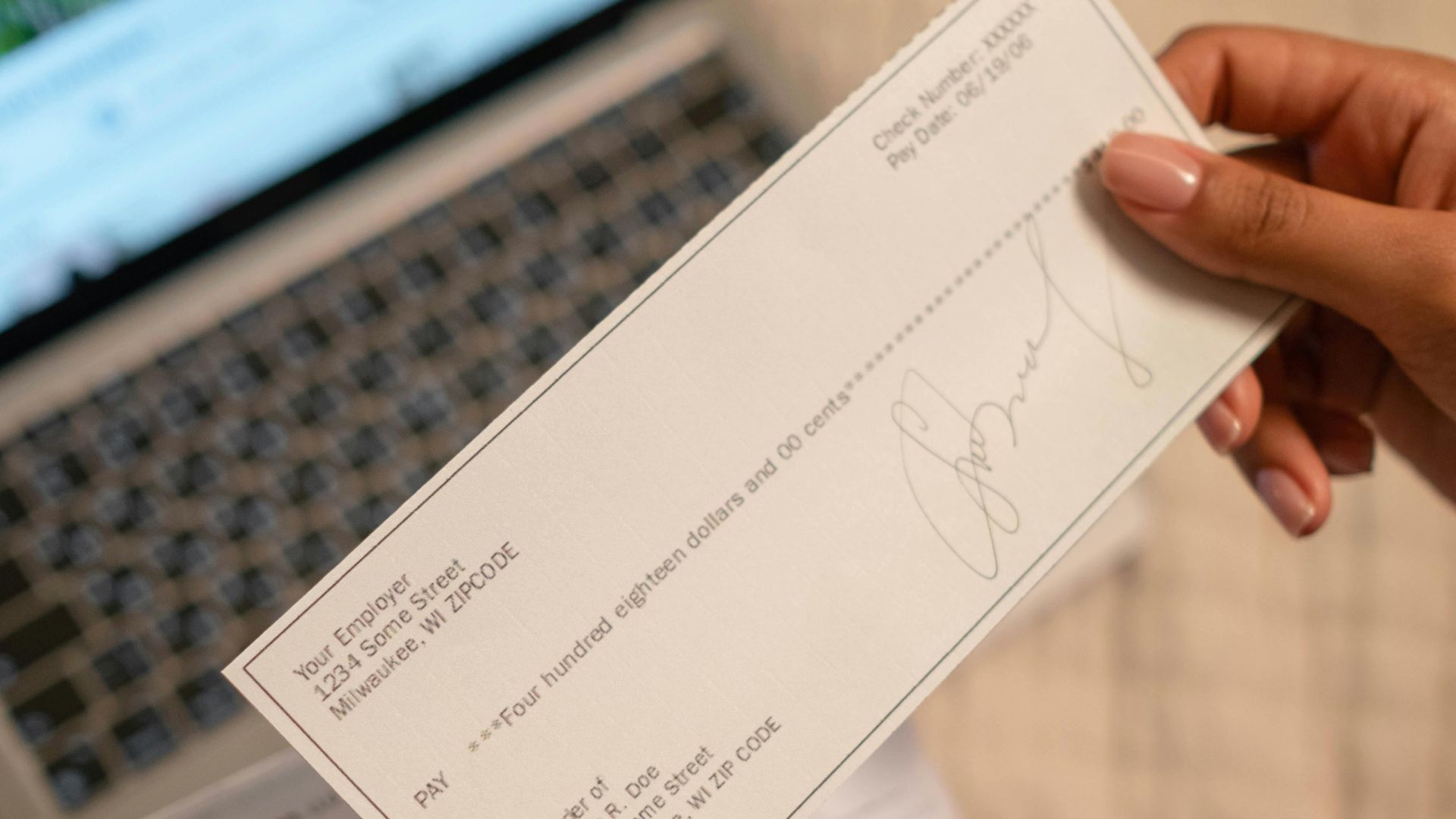 Individual holding a cheque over laptop, signifying online banking or financial transaction.
