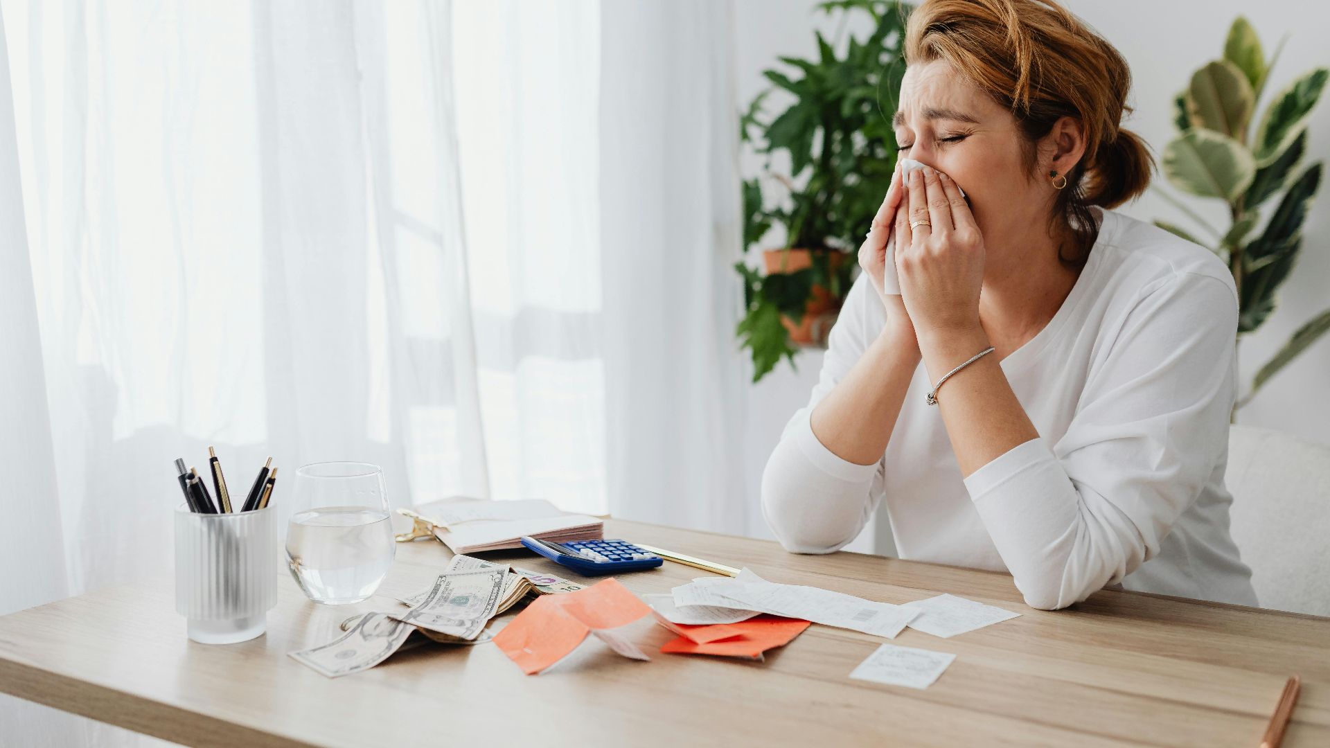 Woman looking stressed while managing finances at her office desk with papers and calculator.
