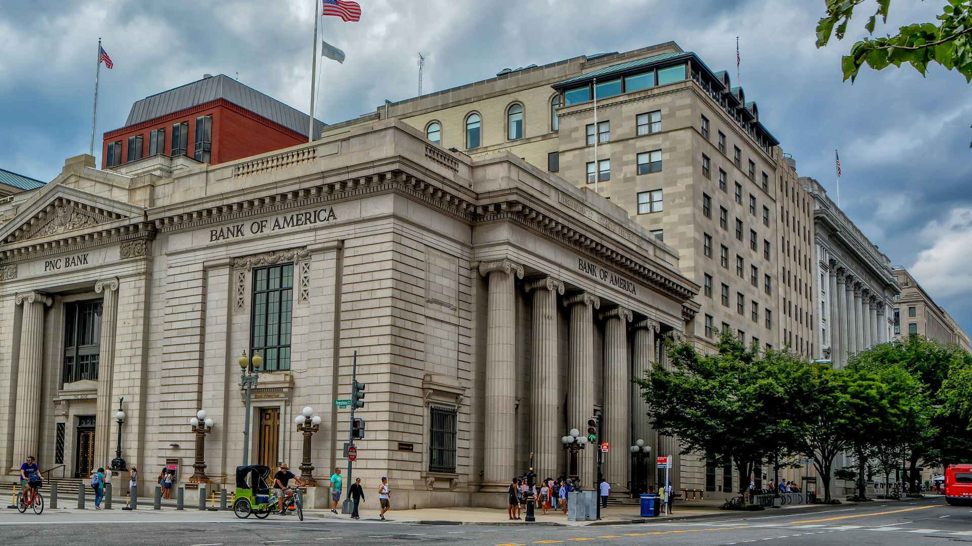 A classic architectural bank building under a dramatic sky in a bustling city environment.