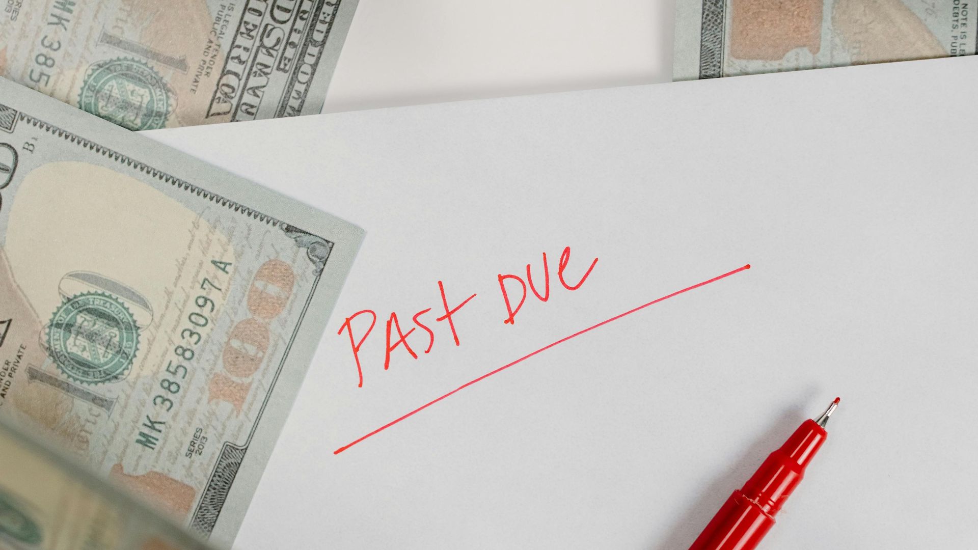 Envelope marked 'Past Due' surrounded by hundred-dollar bills and red pen on white background.