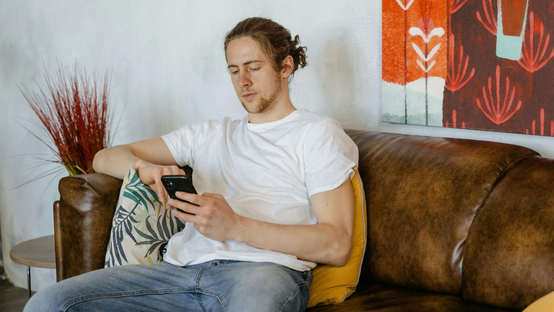 Casual young man in white shirt using smartphone on sofa at home