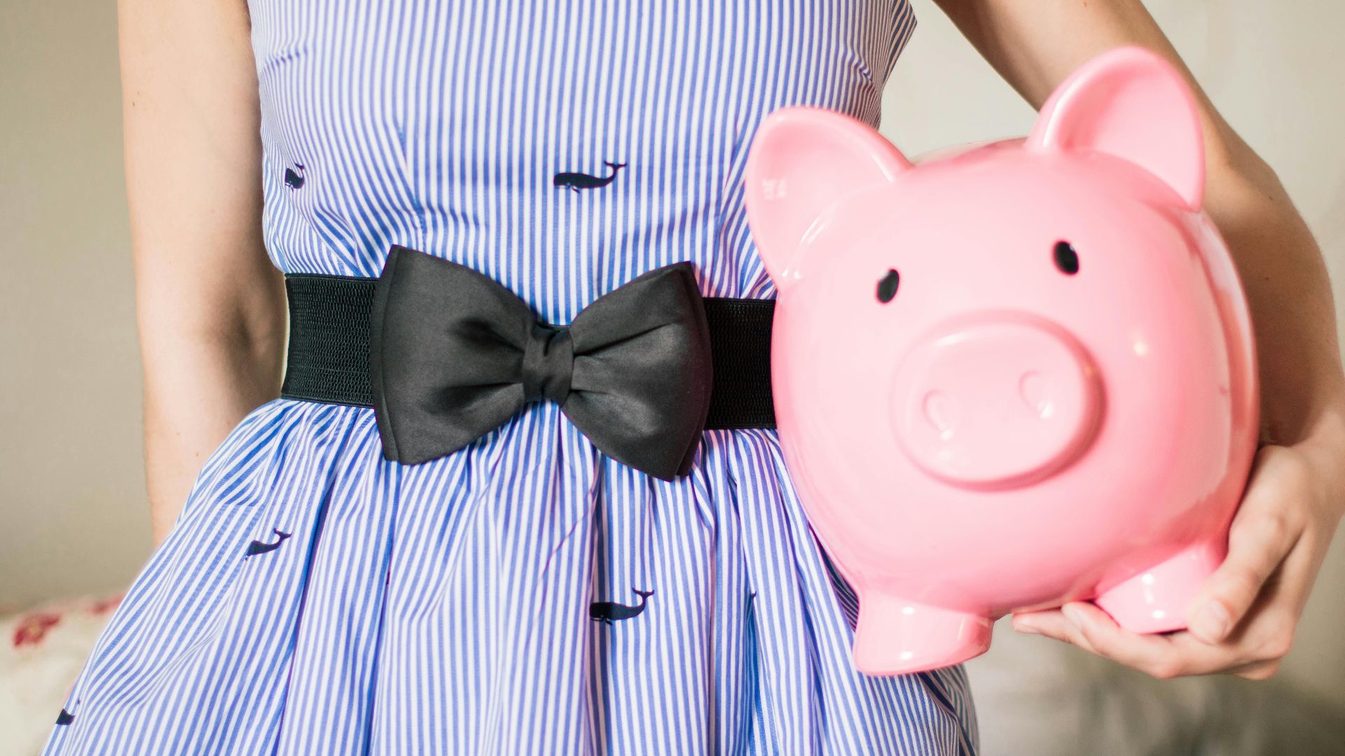 Close-up of a woman in a striped dress holding a pink piggy bank, symbolizing savings and financial planning.