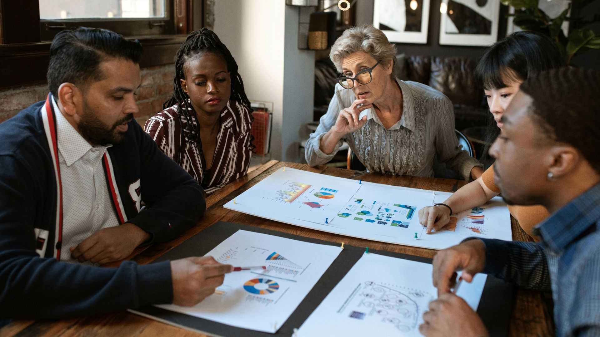 A multicultural team engaged in a business meeting with charts and graphs on the table.