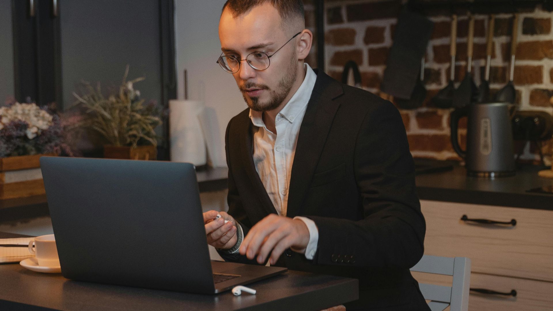 Caucasian man working remotely on a laptop in a cozy kitchen setting.