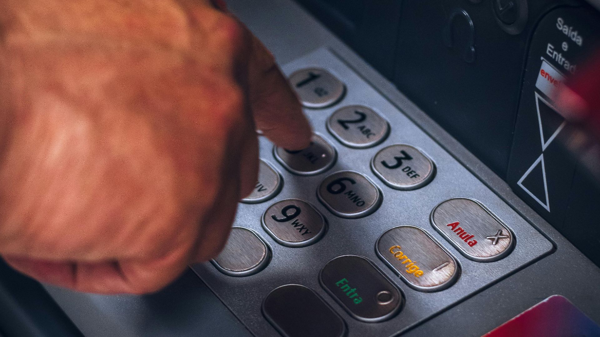 Hand pressing keypad of an ATM in Brazil, emphasizing modern banking technology.