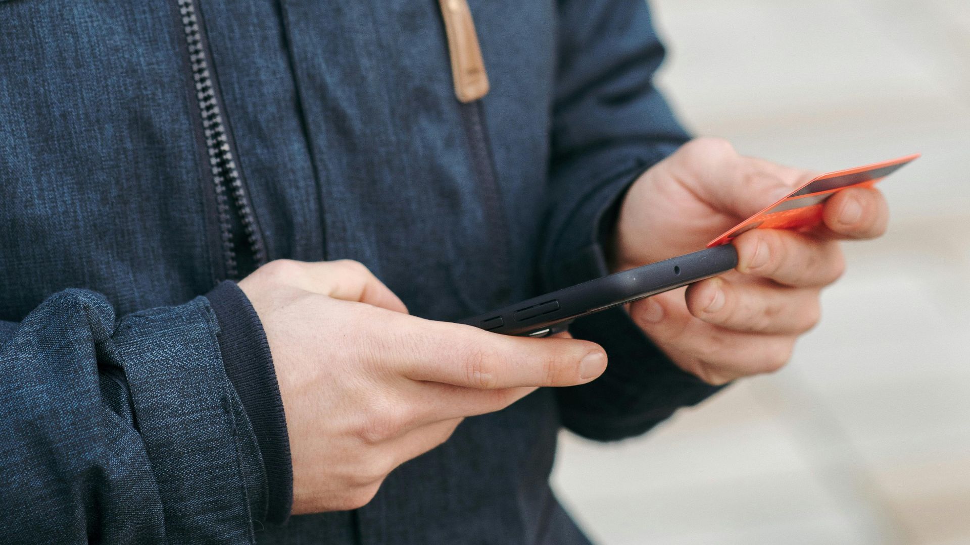 A young man using his smartphone and credit card outdoors for a transaction.