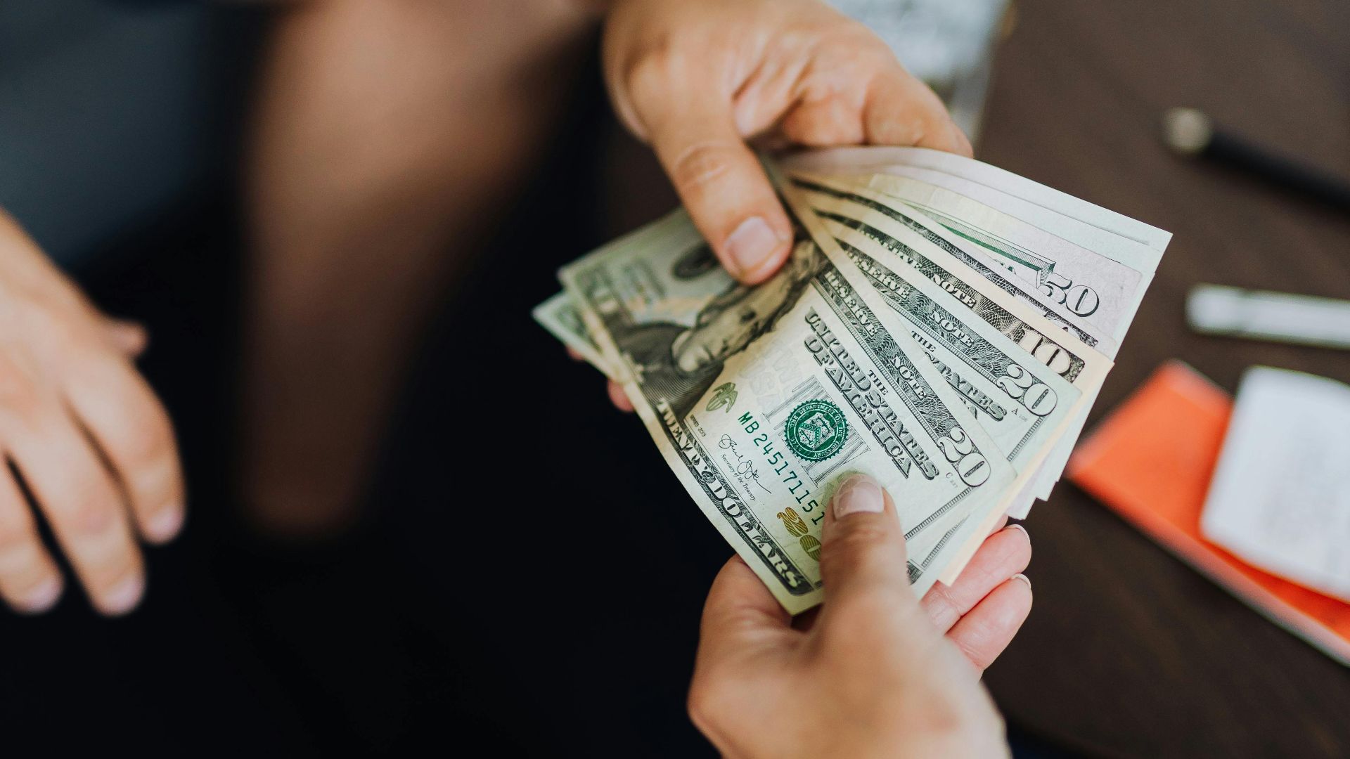 A close-up view of hands exchanging dollar bills indoors, symbolizing payment.