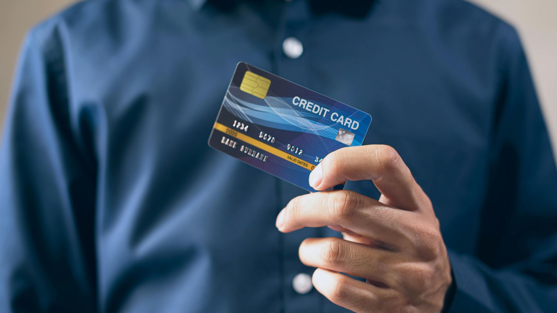 Close-up of a person holding a credit card in a hand, wearing a button-up shirt.