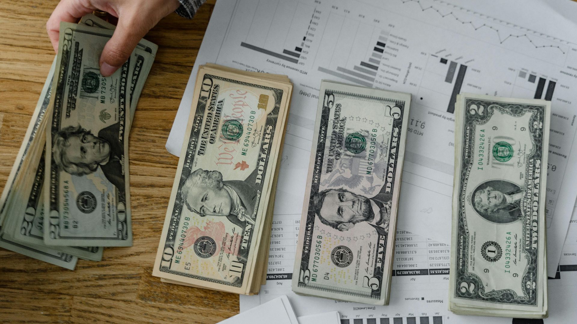 Person holds US dollars over financial papers, showing income or budget analysis.
