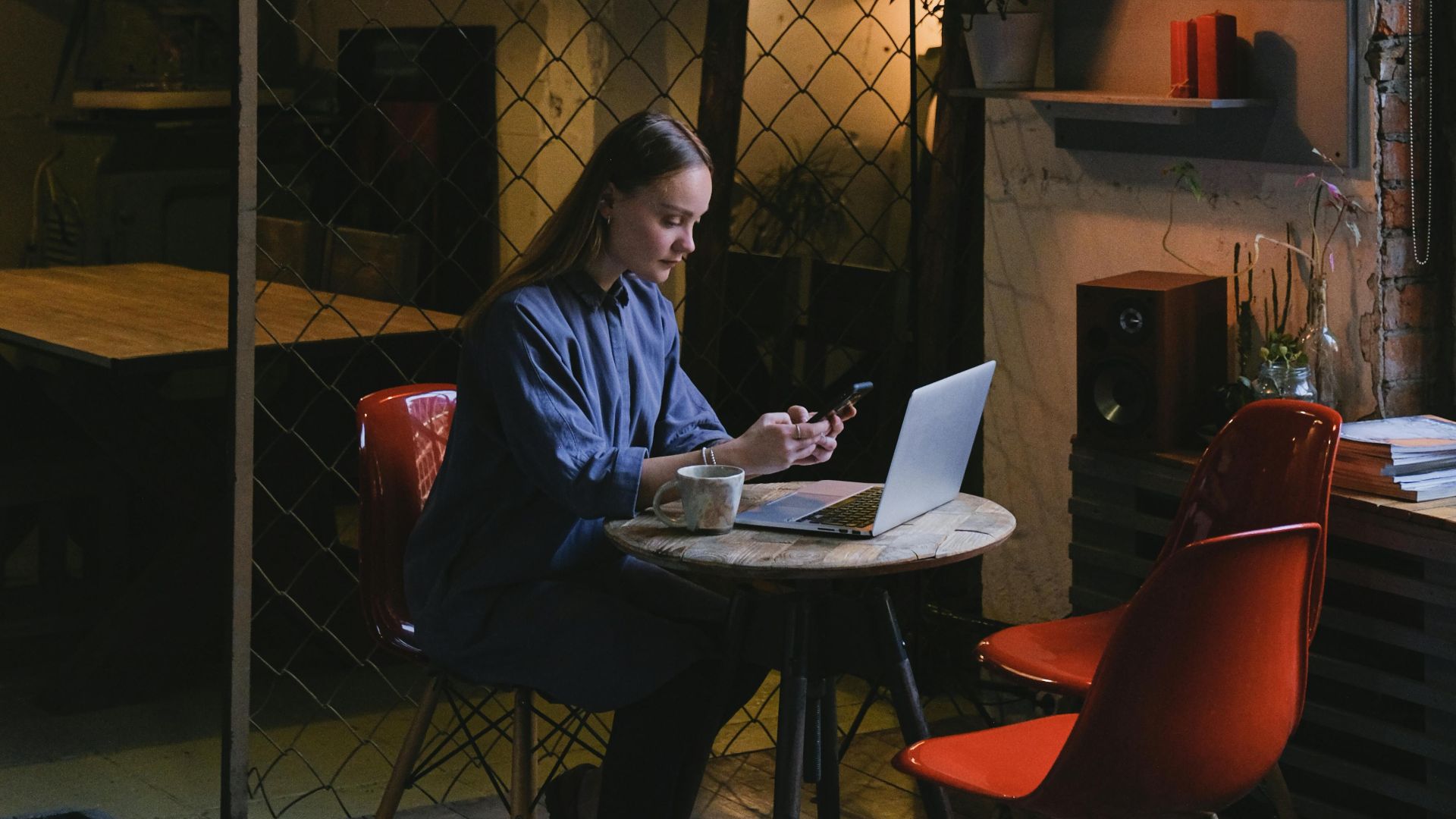Woman in a cozy café using a laptop and smartphone. Warm lighting creates an inviting atmosphere.