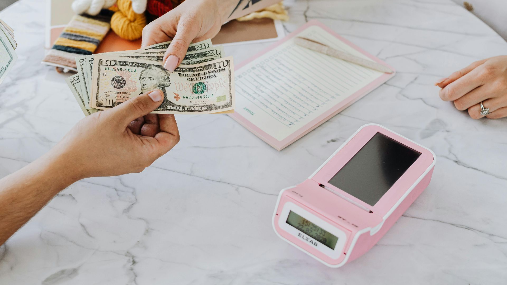 Close-up of hands exchanging US dollars over a marble table with a card reader.