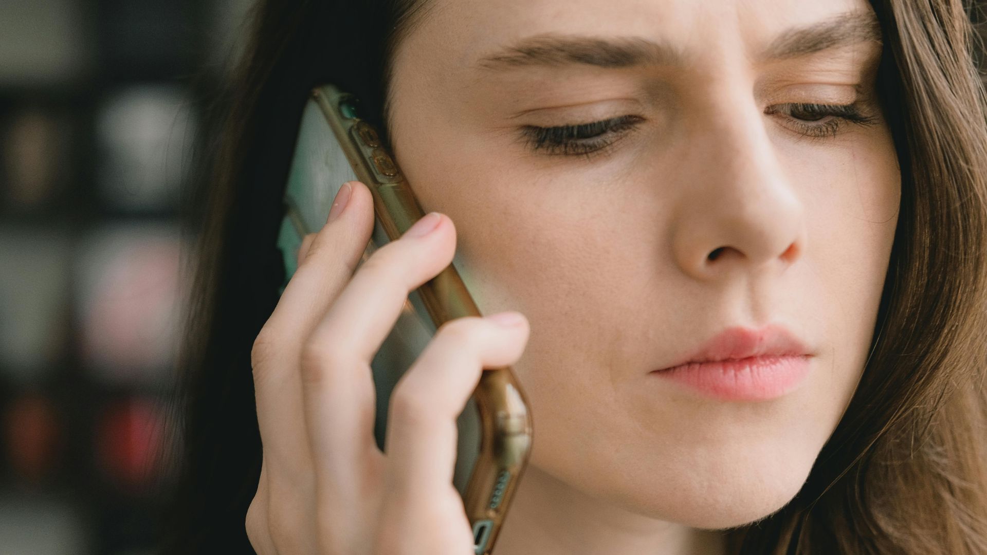 Close-up of a woman engaged in a phone conversation indoors, depicting a thoughtful expression.