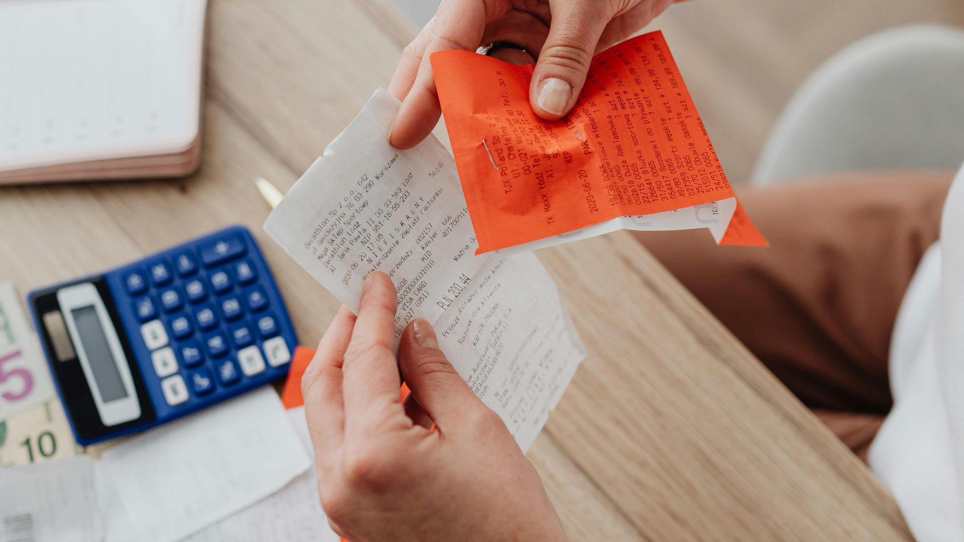 Top view of person organizing finances with calculator, receipts, and notes at desk.
