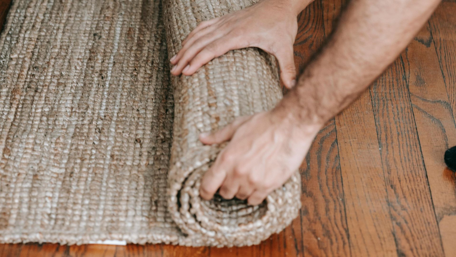 Couple rolling up a beige carpet on wooden floor, preparing for moving day.