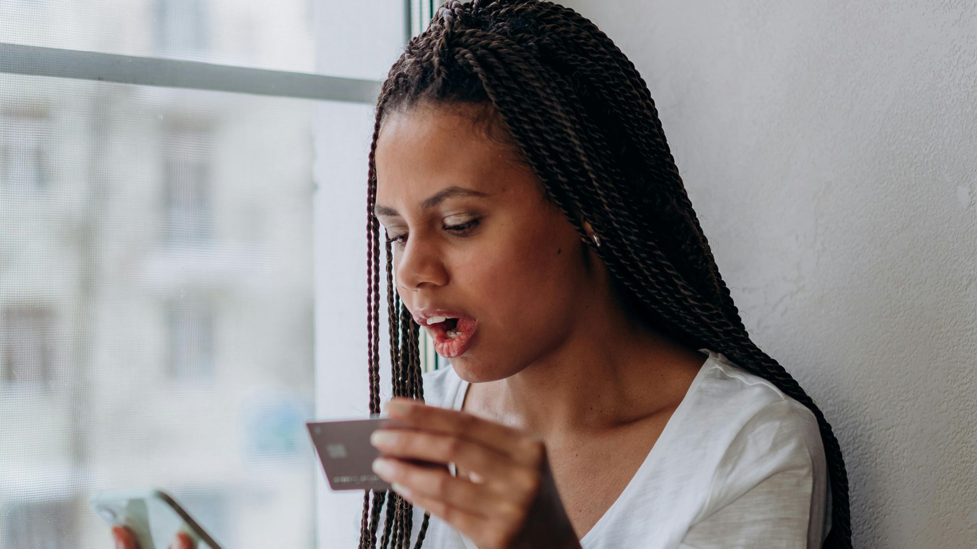 African woman using smartphone and credit card at home.