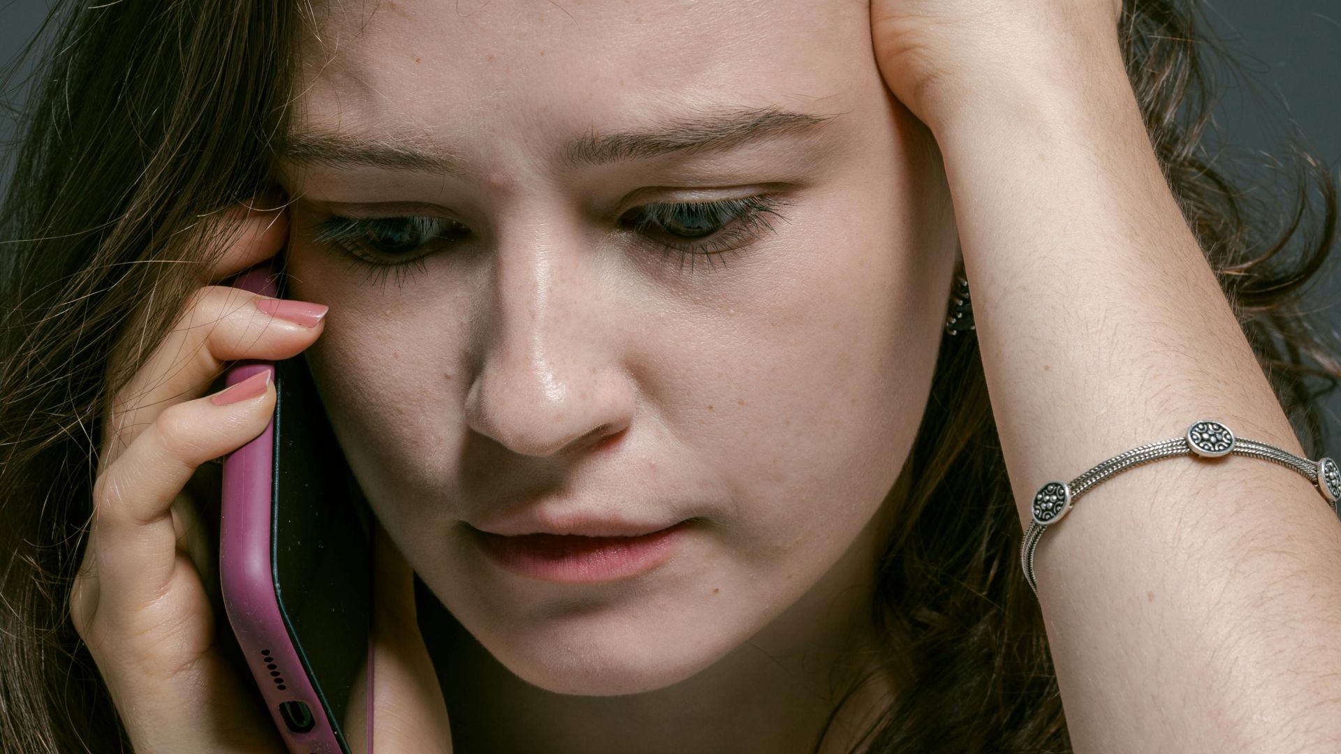 Close-up of a young woman looking worried while holding a smartphone to her ear.