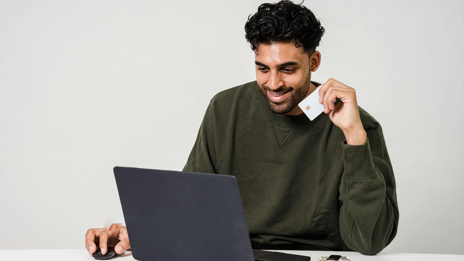 A man smiling while using a laptop and holding a credit card for online shopping.